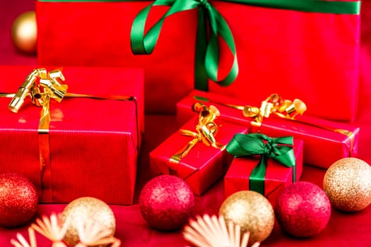 Five red Christmas presents placed on a red cloth. Bows in green and gold. Baubles and straw stars outside narrow depth of field. Tightly framed, close up. Focus on emerald bow around little red box.