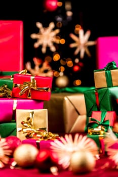 Many unicolored Christmas gifts piled up either side of the tight frame. Shallow depth of field with focus on the golden bow around the small red present. Blurred baubles and stars in front and rear.