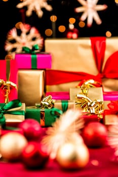 Plain Christmas gifts placed on a red cloth. All with bows and ribbons. Shallow depth of field. Tightly framed. Blurred shapes of baubles and stars in front and back. Bokeh before dark background.