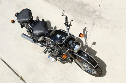 Looking down on a two seat vintage motorcycle outdoors in the sunshine, on cement.