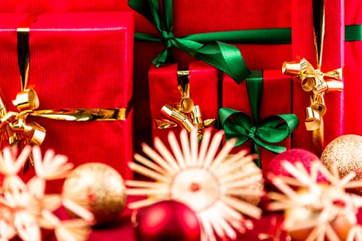 Christmas presents wrapped all in red. Green and golden bows. Blurred stars and baubles in front. Tightly framed. Flattened space. Narrow depth of field. Focus on emerald bow around smallest red box.