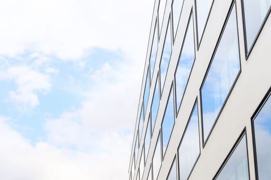 Blue sky and clouds reflected in mirrored windows of new modern building glass facade. Background with free copy-space area for your text.