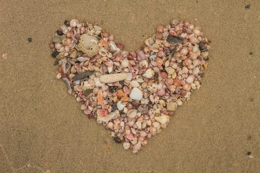 Heart made of sea shells lying on a beach sand in summer