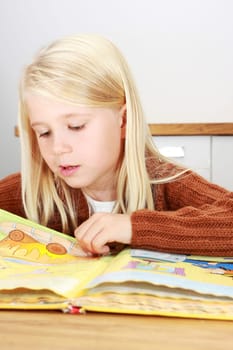 Young blond first grade girl reading a book for her homework