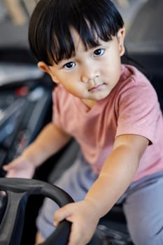 A cute little boy is sitting at the wheel of a lawnmower and looking into the camera.
