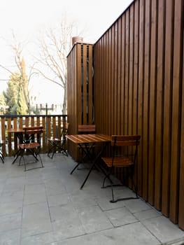 Vertical photograph of summer cafe with wooden chairs and tables. Nice outdoor cafe made of wood. Eating on terrace in good weather. Simple cafe on street to relax while walking around city
