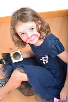 Little cute girl using make-up to turn herself into clown