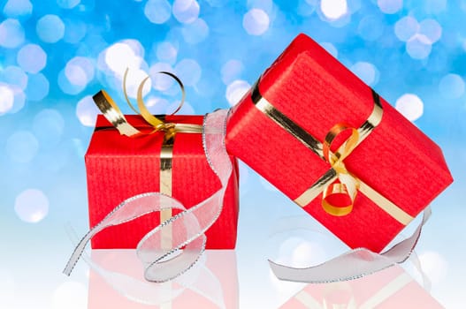 Color photo of two red and gold gift boxes with a flowing silver ribbon on a background consisting of  out of focus lights on blue.