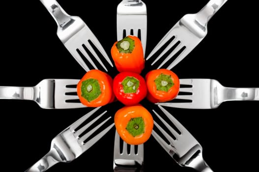 Still-life of Colorful peppers and shiny silver forks isolated on a black background