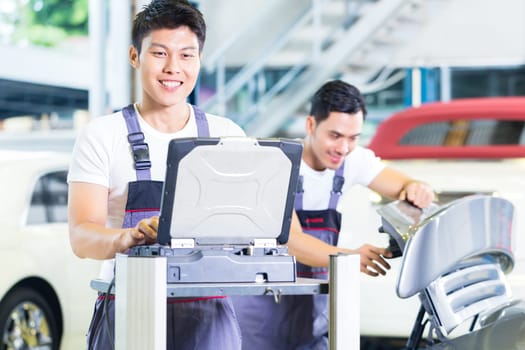 Asian Chinese car mechanics checking auto engine with diagnostics tool in his workshop