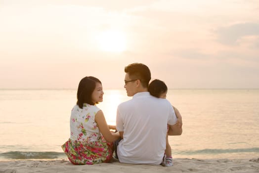 Portrait of young Asian family seated on beach outdoor vacation, during summer sunset, natural sunlight.