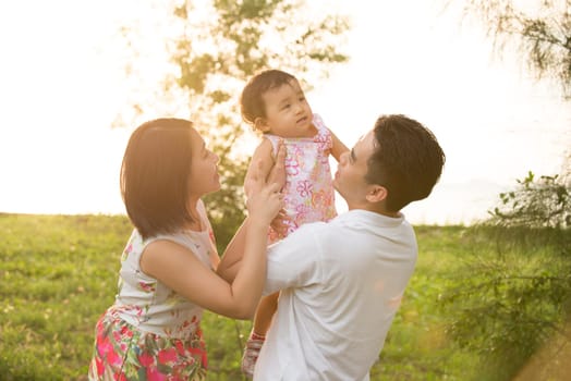Portrait of joyful happy Asian family playing together at outdoor park during summer sunset.