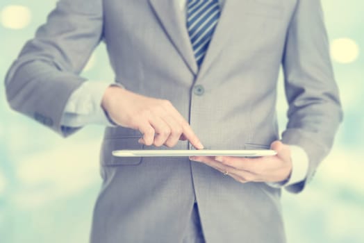Close-up of male hands touching digital tablet, formal businessman standing with blur background.