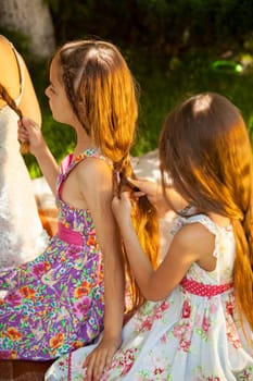 Two little girls sitting outdoor and doing hairstyles at park