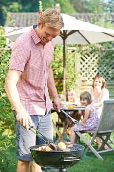 Father Cooking Barbeque For Family In Garden At Home