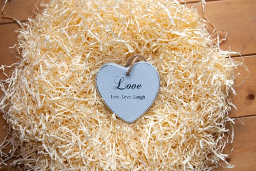 single grey wooden love heart in a love nest made of straw inscribed  love, live and laugh