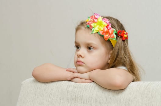The girl thoughtfully looks to the left, his arms dangling from the back of the couch, and laid on the sofa his head. On the head of a girls band with beautiful flowers