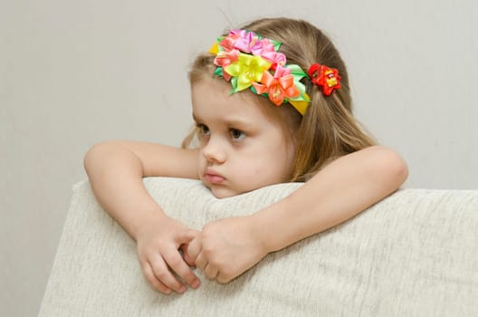 The girl thoughtfully looks to the left, his arms dangling from the back of the couch, and laid on the sofa his head. On the head of a girls band with beautiful flowers