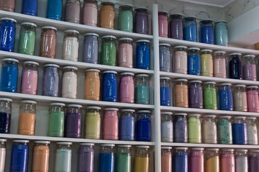 Shelves filled with rows of glasses of colorful pigments in a pharmacy artist's supplies in Marrakech as a close-up