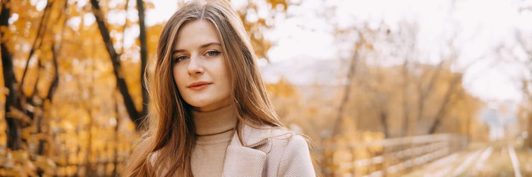 A beautiful long-haired woman walks through the autumn streets. Railway, autumn leaves, a woman in a light coat.