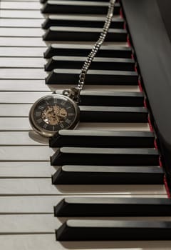 Antique pocket watch on piano keyboard. Time for music conceptual. Space for text, Selective focus.