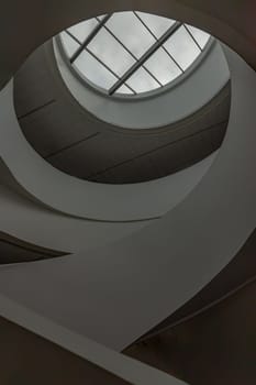 Looking up to the sky through modern channel round circular ceiling with spiral staircase. The white ceiling with Huge transparent circular glass panel on the middle as a main skylight showing sky above, Glass ceiling, Space for text, Selective Focus.