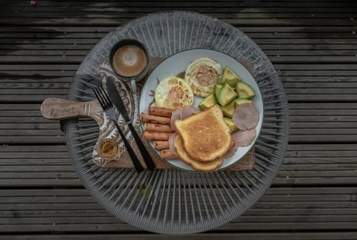 Breakfast is including Fried sausages, Fried eggs, Toast breads and cut avocados served with Honey and Cup of coffee. Top view, Space for text, Selective focus.