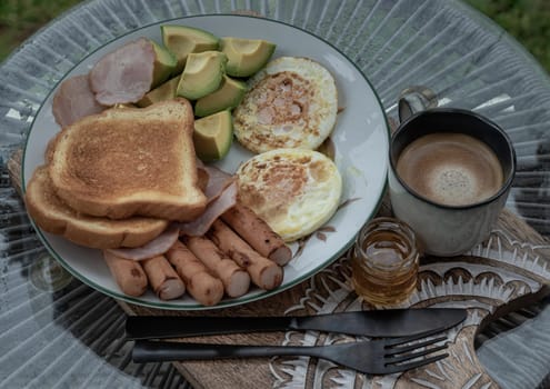 Breakfast is including Fried sausages, Fried eggs, Toast breads and cut avocados served with Honey and Cup of coffee. Oblique view from the top, Space for text, Selective focus.