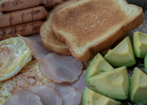 Close-up of Breakfast is including Fried sausages, Fried eggs, Toast breads and cut avocados. Space for text, Selective focus.