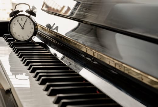 Black alarm clock stand on the Piano Keyboard. Time for music concept. Space for text, Selective focus.
