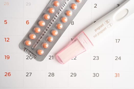 Pregnancy test and birth control pills on calendar, contraception health and medicine.