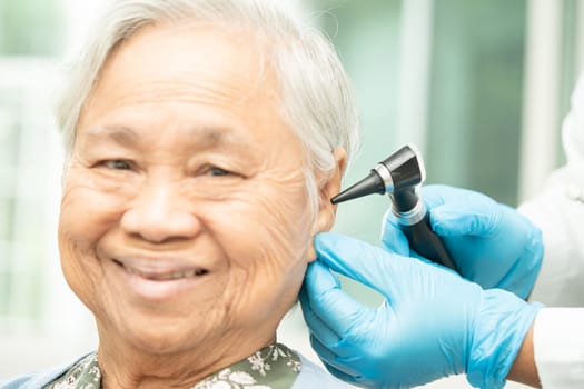 Audiologist or ENT doctor use otoscope checking ear of asian senior woman patient treating hearing loss problem.