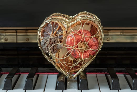 Golden heart shaped mesh case is filled with dried fruits stand on the Piano Keyboard. Dried fruits in heart shaped metal case on keyboard, Christmas decoration, Melody of Love concept, Space for text, Selective focus.