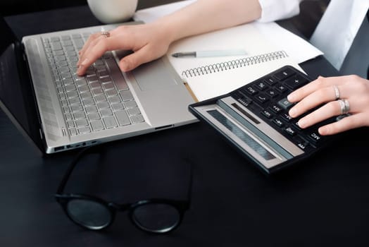 Efficient Accounting: Woman Uses Calculator and Laptop in Office, Embracing Finance and Accounting, Even When Working from Home.