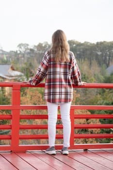 back view of unrecognizable Woman in red plaid shirt enjoying nature walking in Japanese Garden with red pagoda