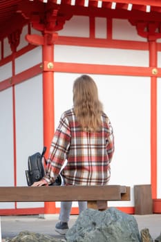 back view of unrecognizable Woman in red plaid shirt enjoying nature walking in Japanese Garden with red pagoda