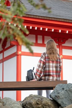 back view of unrecognizable Woman in red plaid shirt enjoying nature walking in Japanese Garden with red pagoda