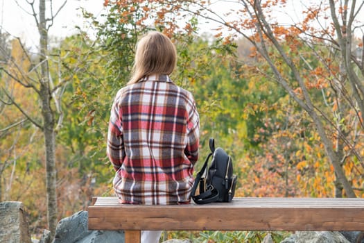 Woman in red plaid shirt enjoying nature sitting in Japanese Garden