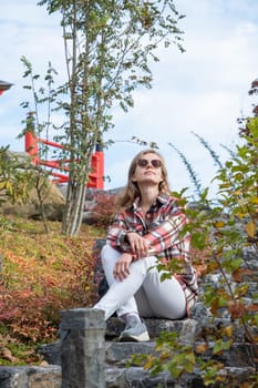 Woman in red plaid shirt enjoying nature sitting in Japanese Garden