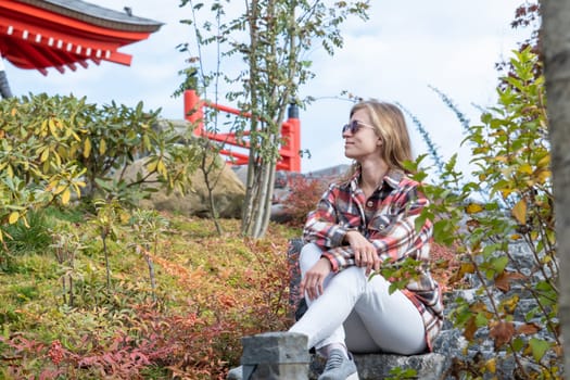 Woman in red plaid shirt enjoying nature sitting in Japanese Garden