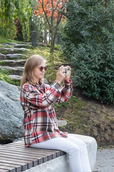 Woman in red plaid shirt enjoying nature standing in Japanese Garden taking photo on smartphone