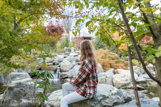 Woman in red plaid shirt enjoying nature sitting in Japanese Garden