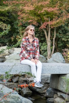 Woman in red plaid shirt enjoying nature sitting in Japanese Garden