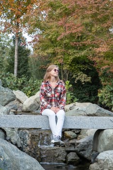 Woman in red plaid shirt enjoying nature sitting in Japanese Garden