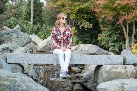 Woman in red plaid shirt enjoying nature sitting in Japanese Garden