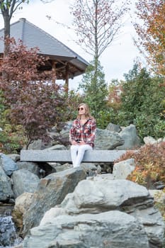 Woman in red plaid shirt enjoying nature sitting in Japanese Garden