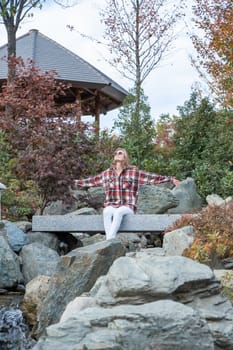 Woman in red plaid shirt enjoying nature sitting in Japanese Garden