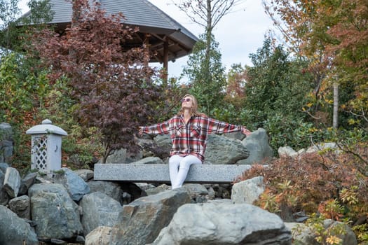 Woman in red plaid shirt enjoying nature sitting in Japanese Garden