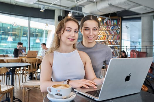Warsaw, Poland, 12.05.2023. Two young teenage females in cafe using laptop, talking. Technologies for leisure communication, study, internet online services, e-shopping