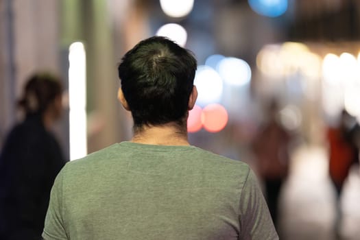 A man is seen walking alone, surrounded by the vibrant night lights of the city.